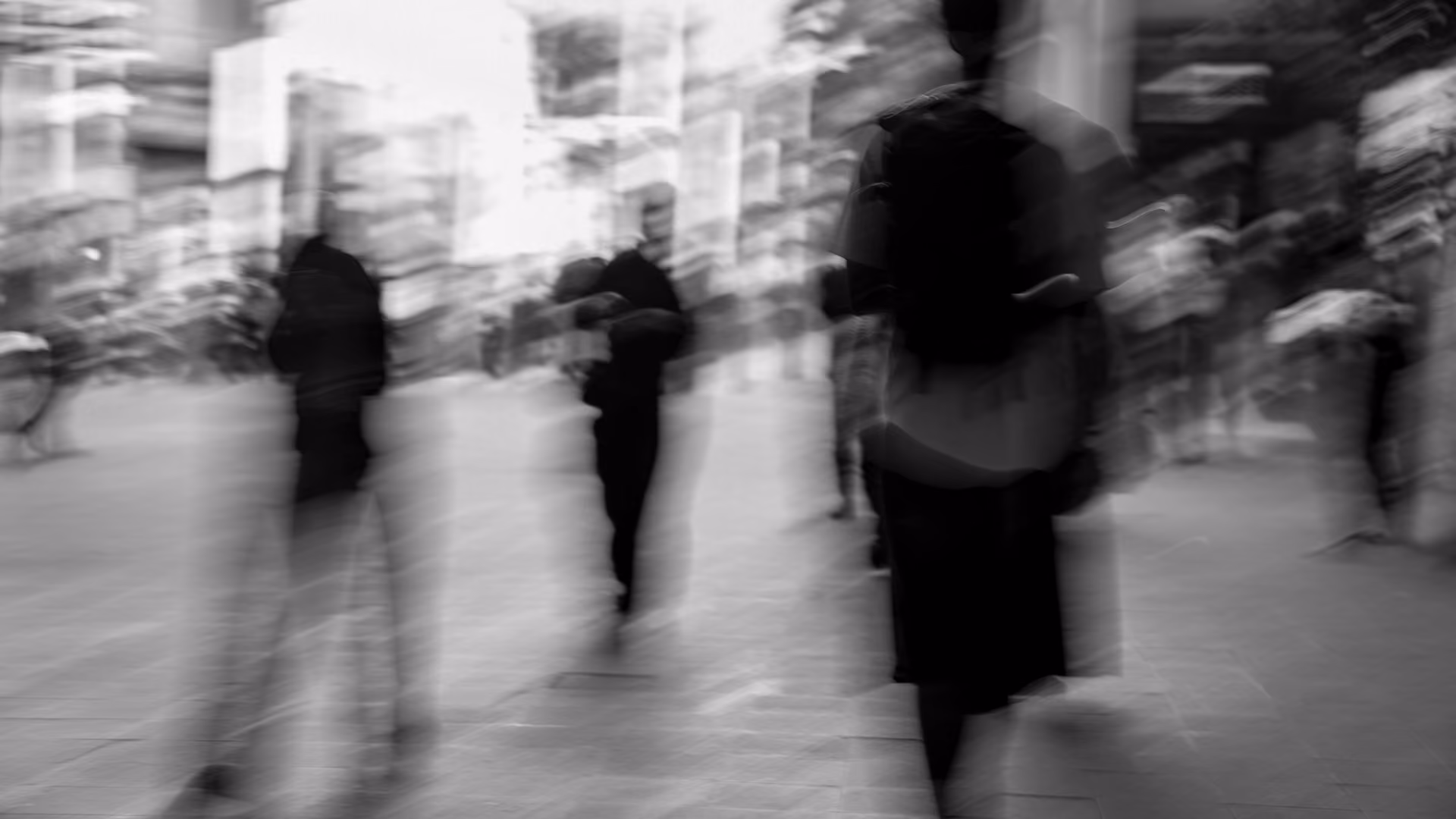 Black and white blurry photo of people walking on a city street, capturing movement and motion with indistinct figures.
