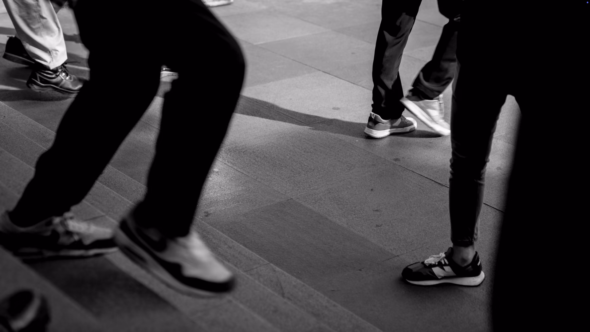 Black and white photo showing several people’s legs and feet walking on paving stones and steps, wearing casual sneakers.