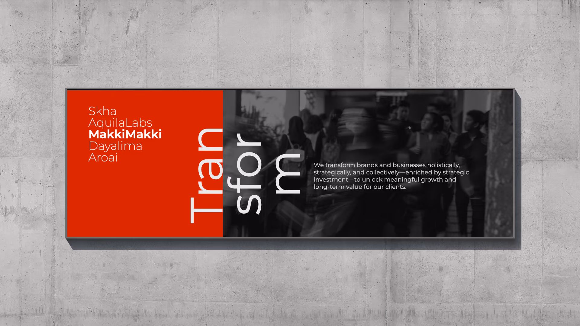 A wall-mounted rectangular sign split into a red left side and a dark right side with a blurred image of people. The red side lists names including Skha, AquilaLabs, MakkiMakki in bold, Dayalima, and Aroai. The dark side shows the word 'Transform' split vertically and a message saying: 'We transform brands and businesses holistically, strategically, and collectively—enriched by strategic investment—to unlock meaningful growth and long-term value for our clients.'