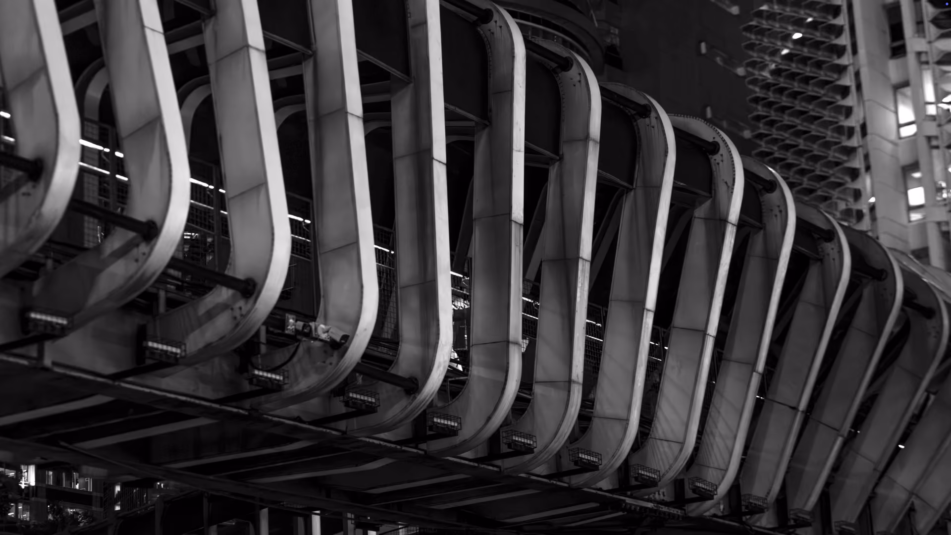 Black and white photo showing a close-up of a modern bridge with curved, repeating structural supports at night.
