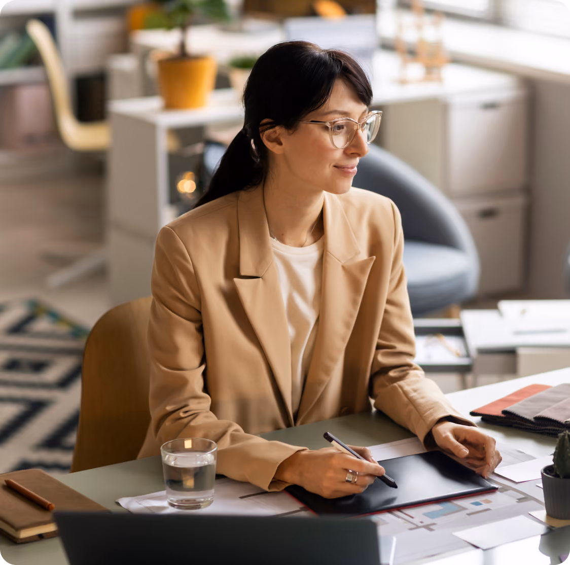 Designerin mit Brille arbeitet konzentriert an einem Grafiktablett an ihrem Schreibtisch im Büro