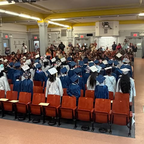 Students in caps and gowns at an indoor graduation ceremony