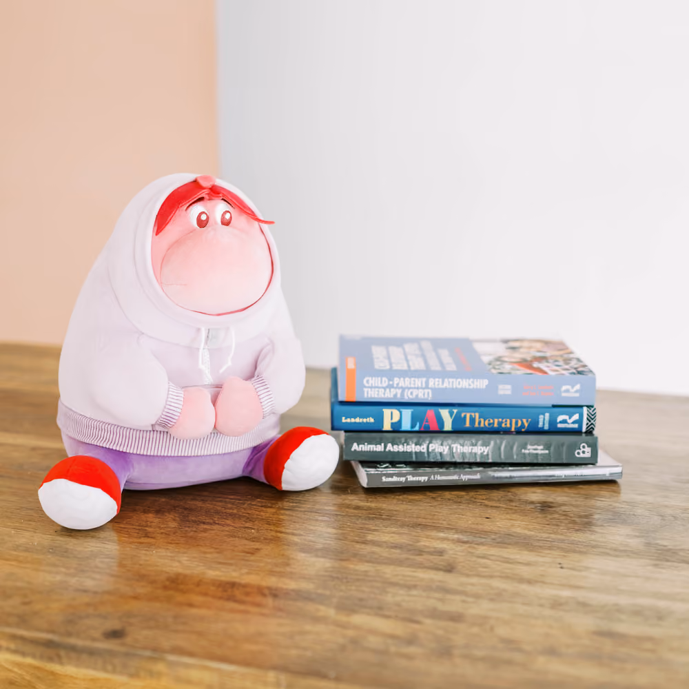 Plush doll in hoodie sitting next to a stack of therapy books on a wooden table.