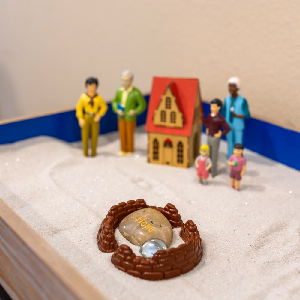 Miniature figures, house, and stone labeled 'Hope' inside a toy sandbox display.