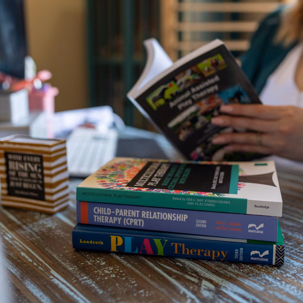 Stack of three therapy books on a table with a person reading a fourth book in the background.