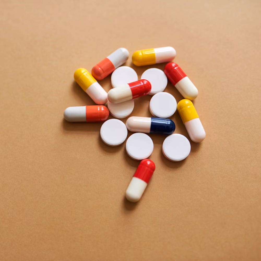 A scatter of white round pills and red, yellow, and blue medicine capsules on a neutral background, illustrating a sticky coping cycle. Shame-free addiction and recovery therapy support from evidence-based mental health professionals at The Desired Journey Counseling.