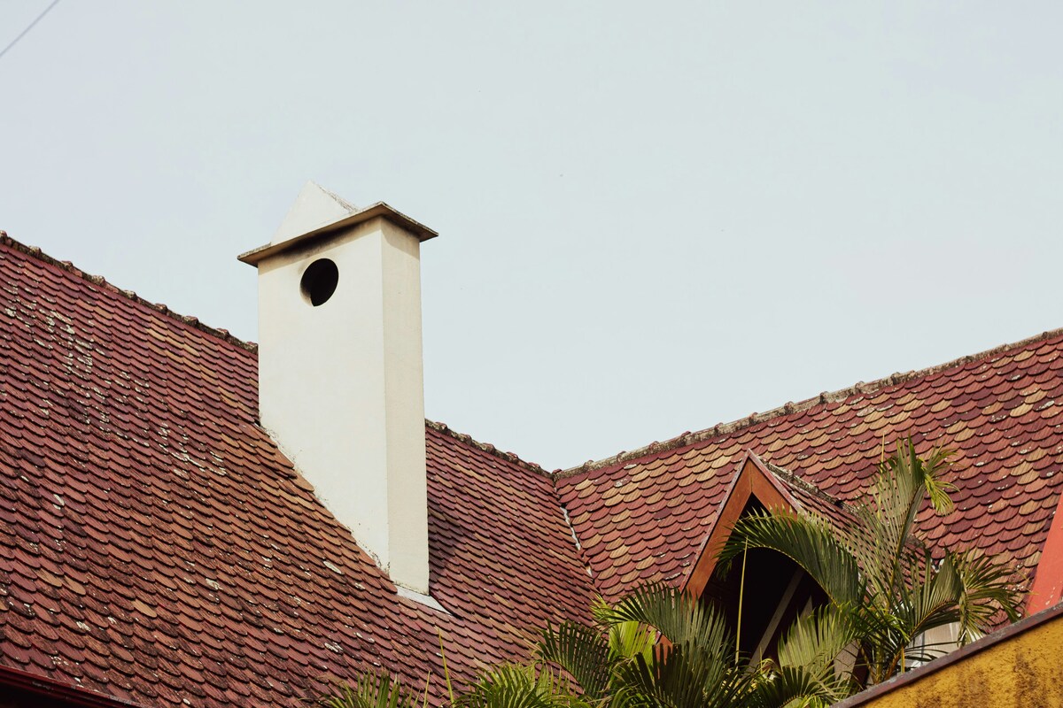 A sturdy roof with red tiles and a white chimney, showcasing a well-maintained home exterior.