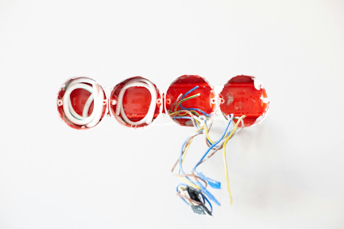 Four red electrical outlet boxes installed in a white wall, with various colored wires emerging from two of the boxes.