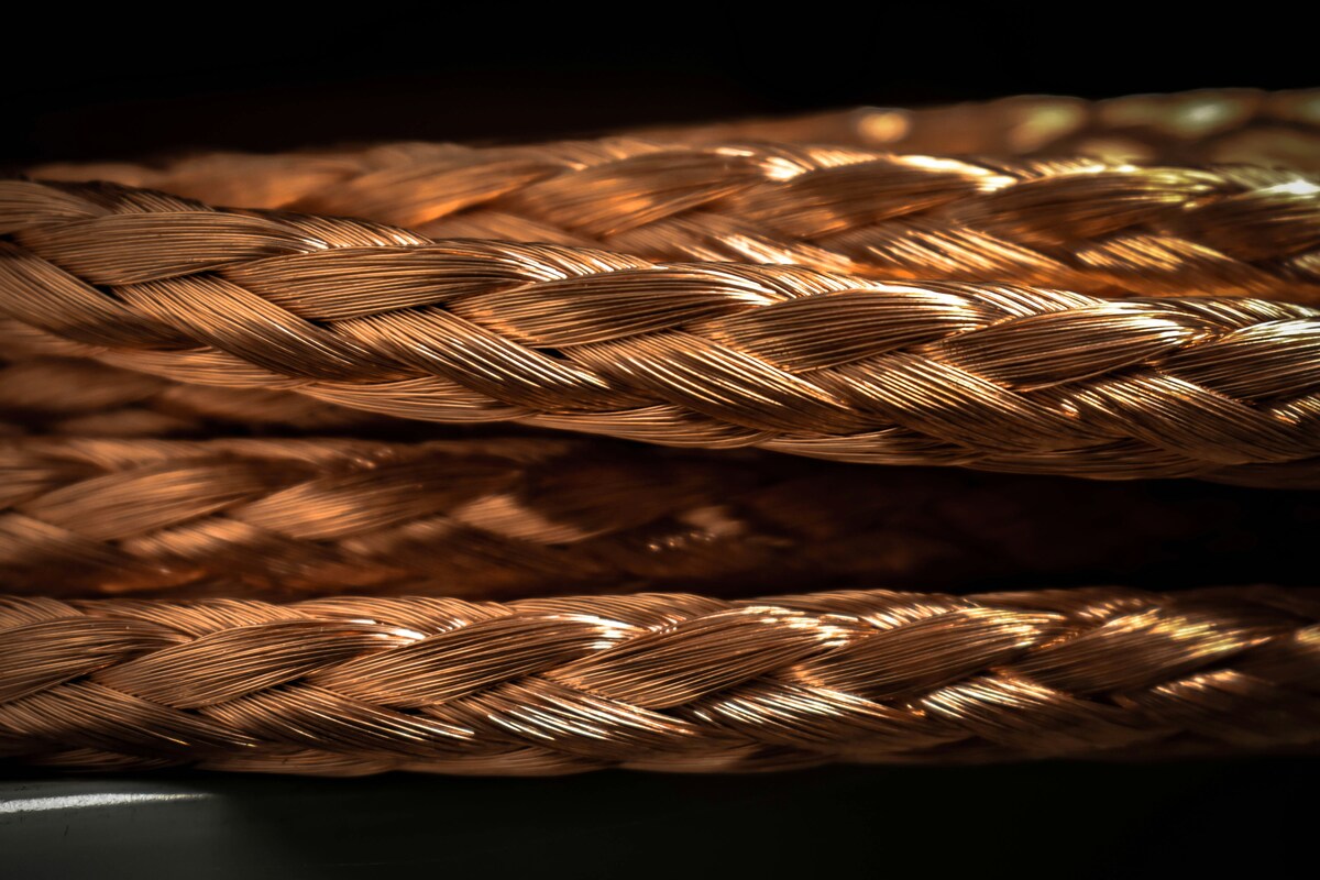 A close-up view of intricately braided copper wires, showcasing their detailed texture and golden hue against a dark background.