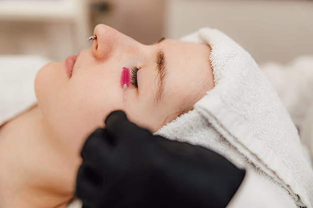 Frau mit Handtuch auf dem Kopf bekommt Wimpernlifting, rechte Wimpern werden gebürstet.