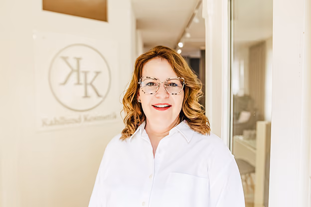 Maike steht vor einer Kosmetikstudio-Wand mit Firmenlogo.