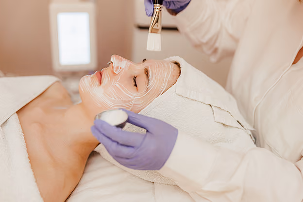 Frau erhält eine Gesichtsbehandlung mit Creme, Gesicht mit Bürste und Handtuch umwickelt.