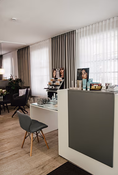 Kosmetikstudio mit moderner Einrichtung, Stuhl, Produkten und großen Fenstern mit Vorhängen.
