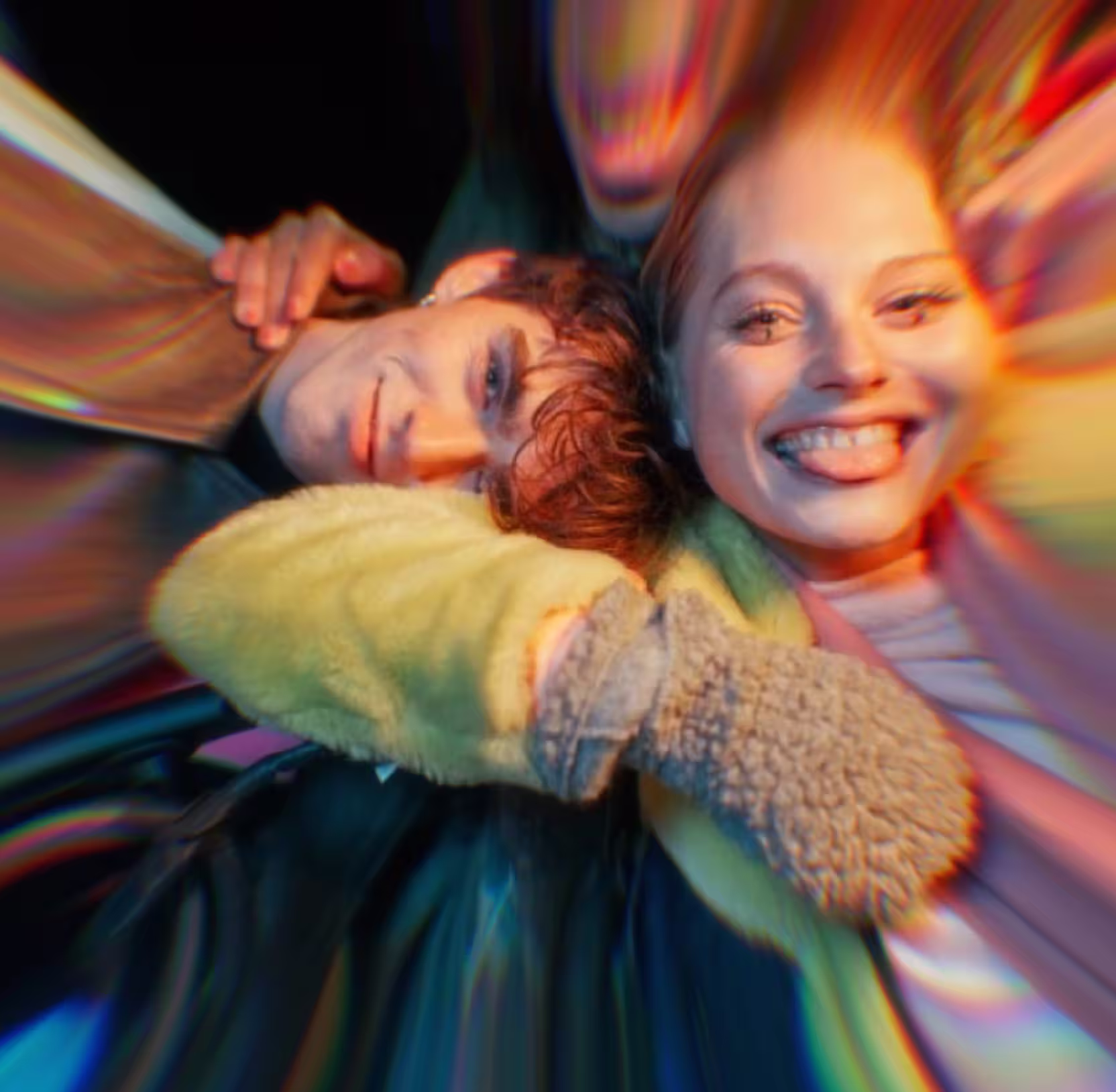 Smiling woman sticking out tongue with arm around a man's neck resting head on her shoulder.