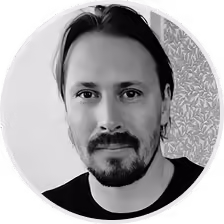 Black and white close-up of man with dark hair, beard, and mustache, neutral expression.
