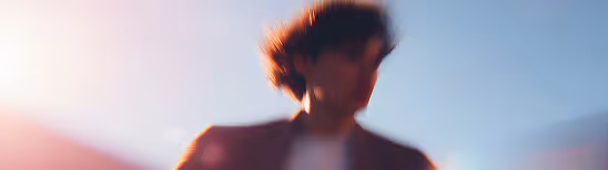 Blurred silhouette of a person with curly hair against a bright sky background.