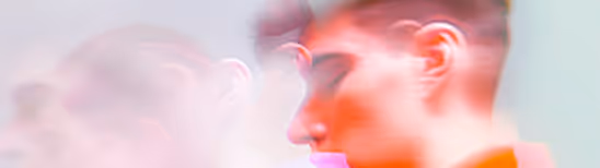 Blurred artistic double exposure of a person’s face with red and pink tones on a light background.
