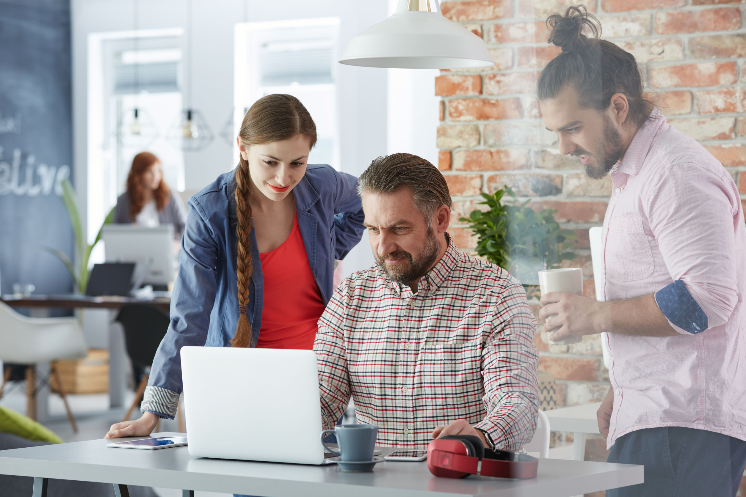 Three people working together at a laptop in a bright office