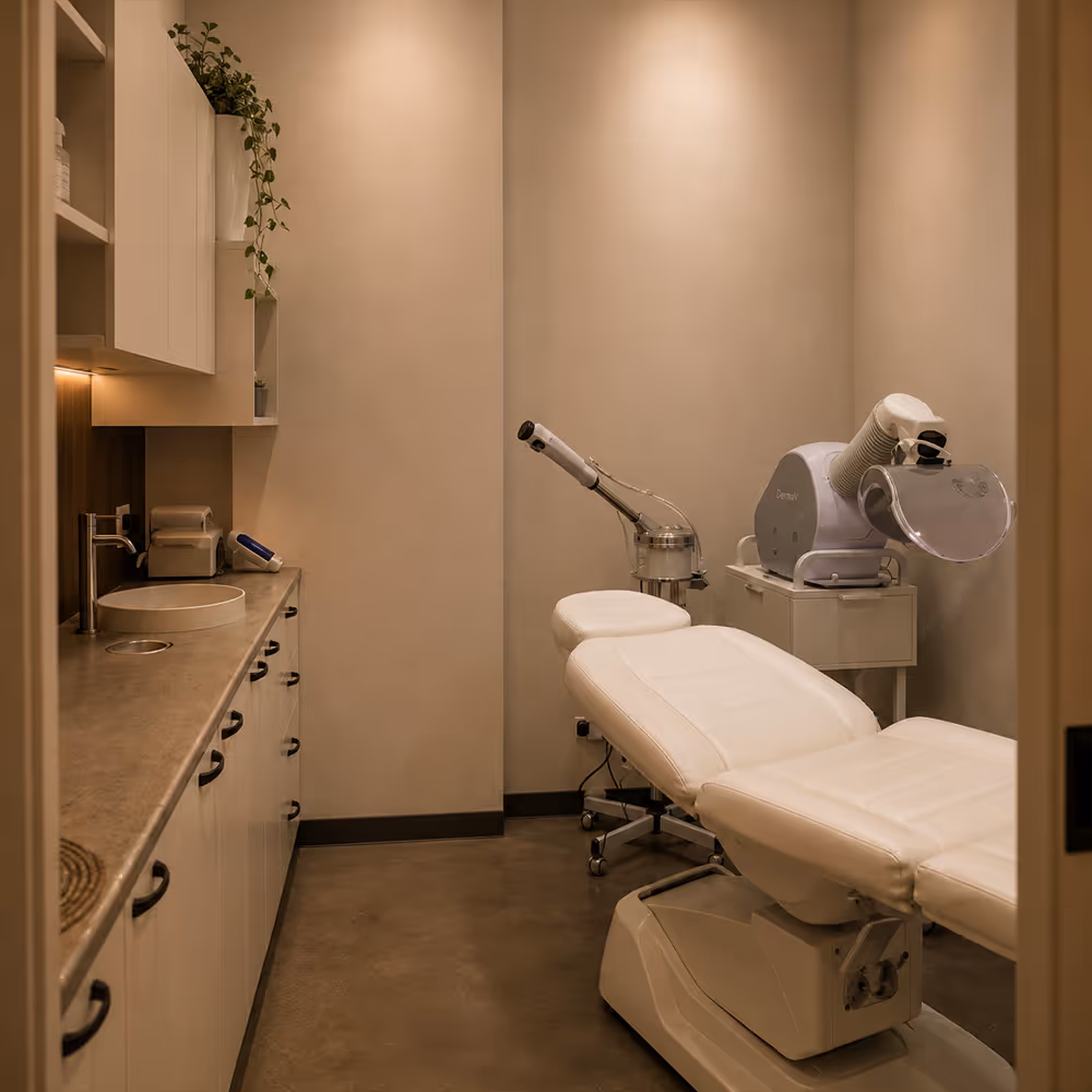 Clinic room with a white adjustable treatment chair and medical devices for skincare or therapy.