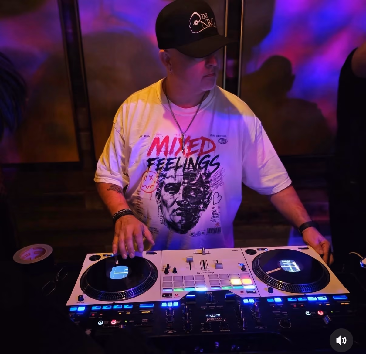DJ wearing a black cap and a Mixed Feelings t-shirt mixes music on a DJ controller with colorful lights.