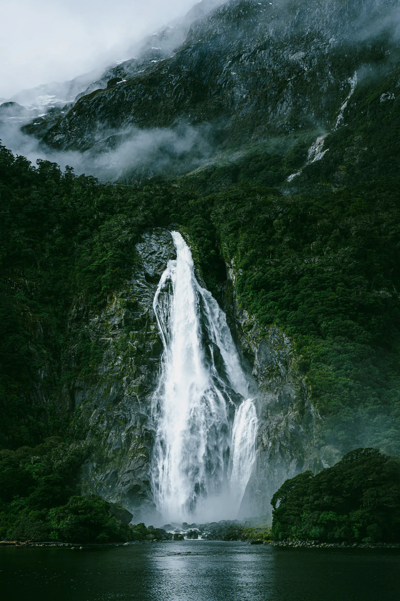 Tall waterfall descending a misty Fiordland mountainside
