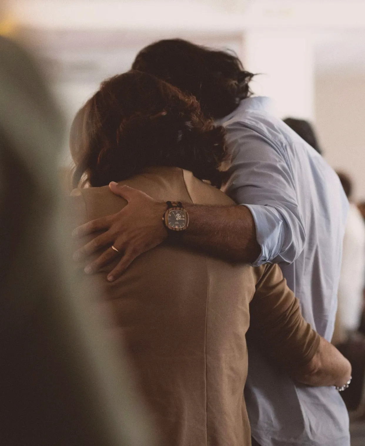 Two people embracing in a warm hug, with others visible in the background.