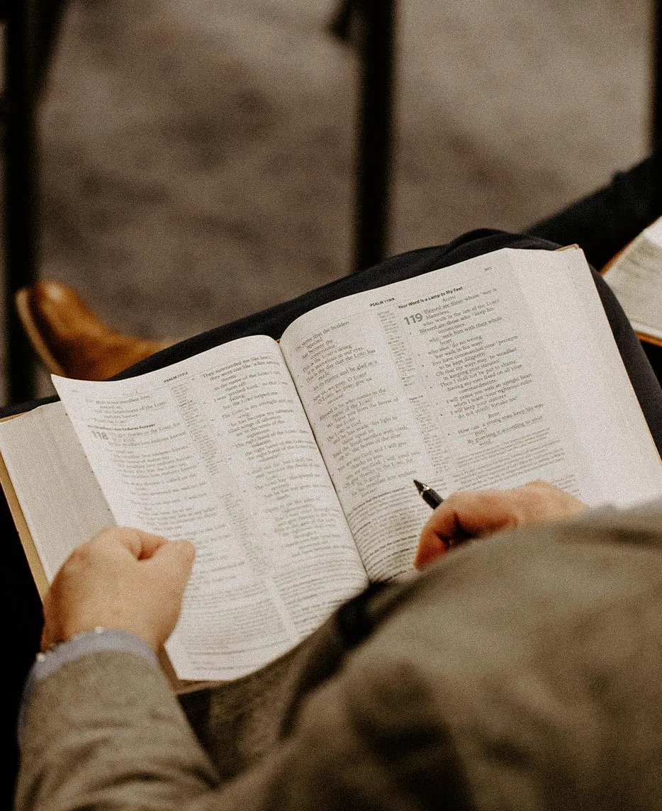 Close-up of hands holding a pen while reading Psalm 119 in an open Bible.