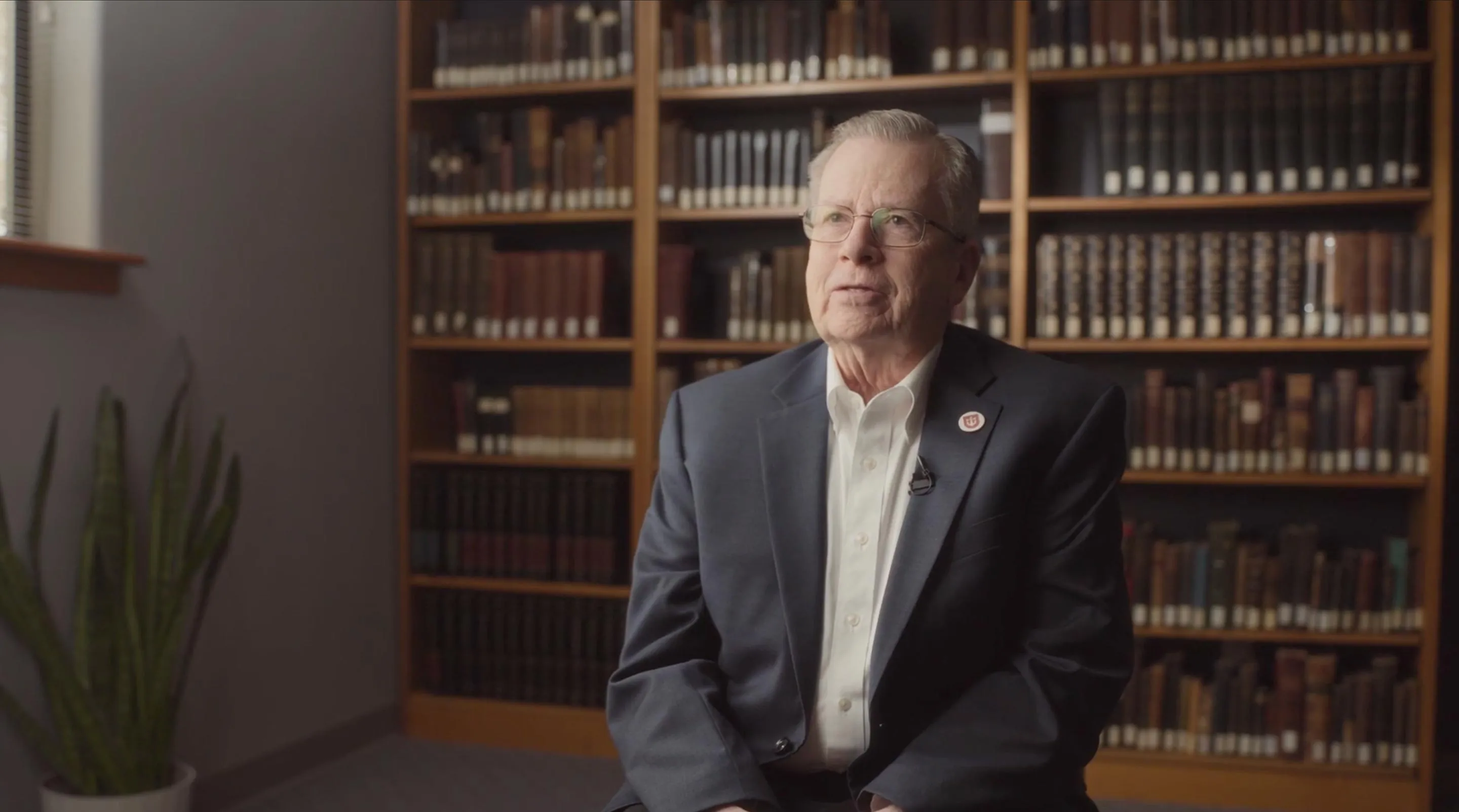 John A. Battle, Professor of New Testament and Theology, speaking during a recorded interview in front of library bookshelves.