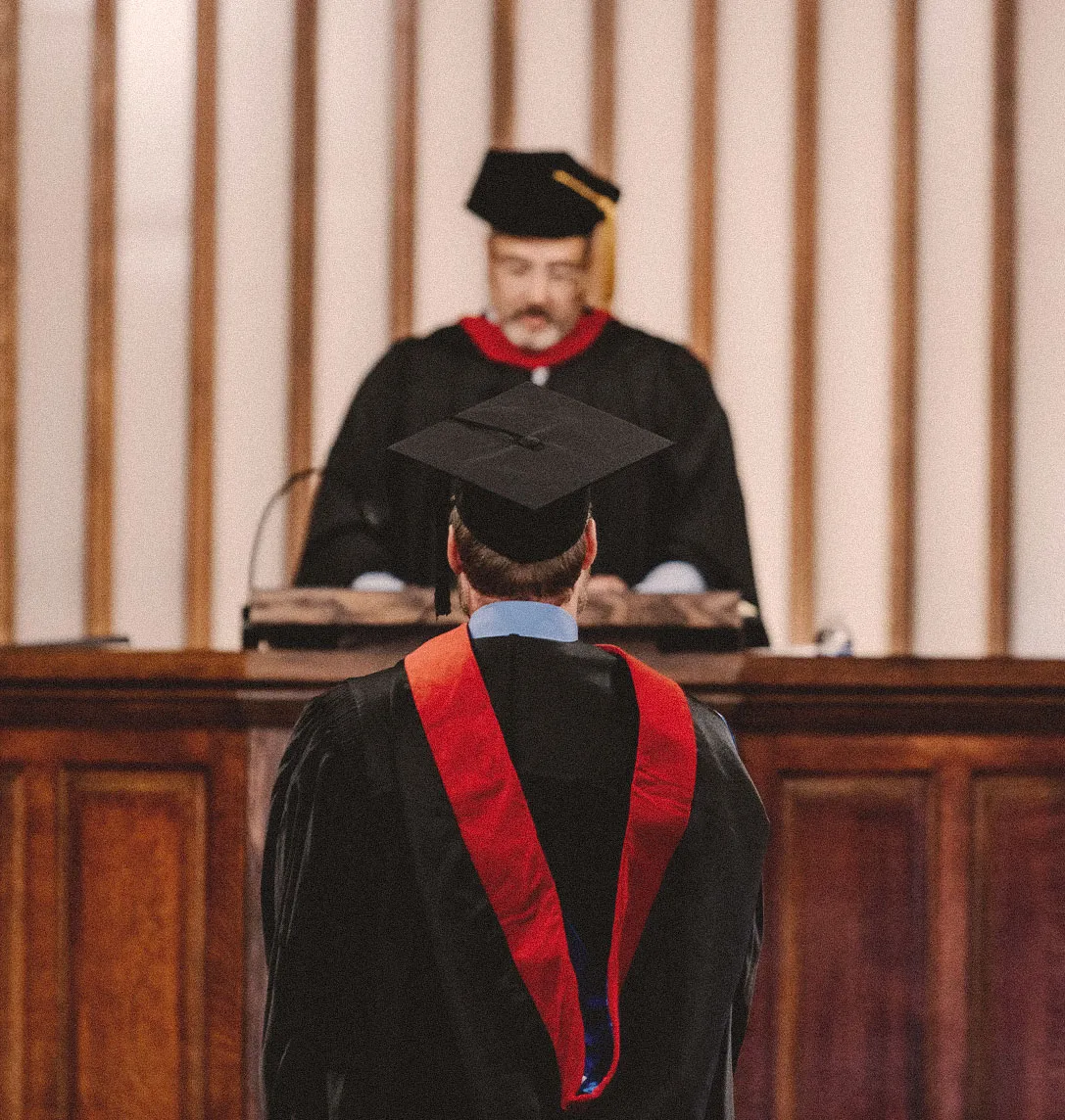 A graduate in cap, gown, and stole standing before a faculty member on the platform during a seminary commencement ceremony.