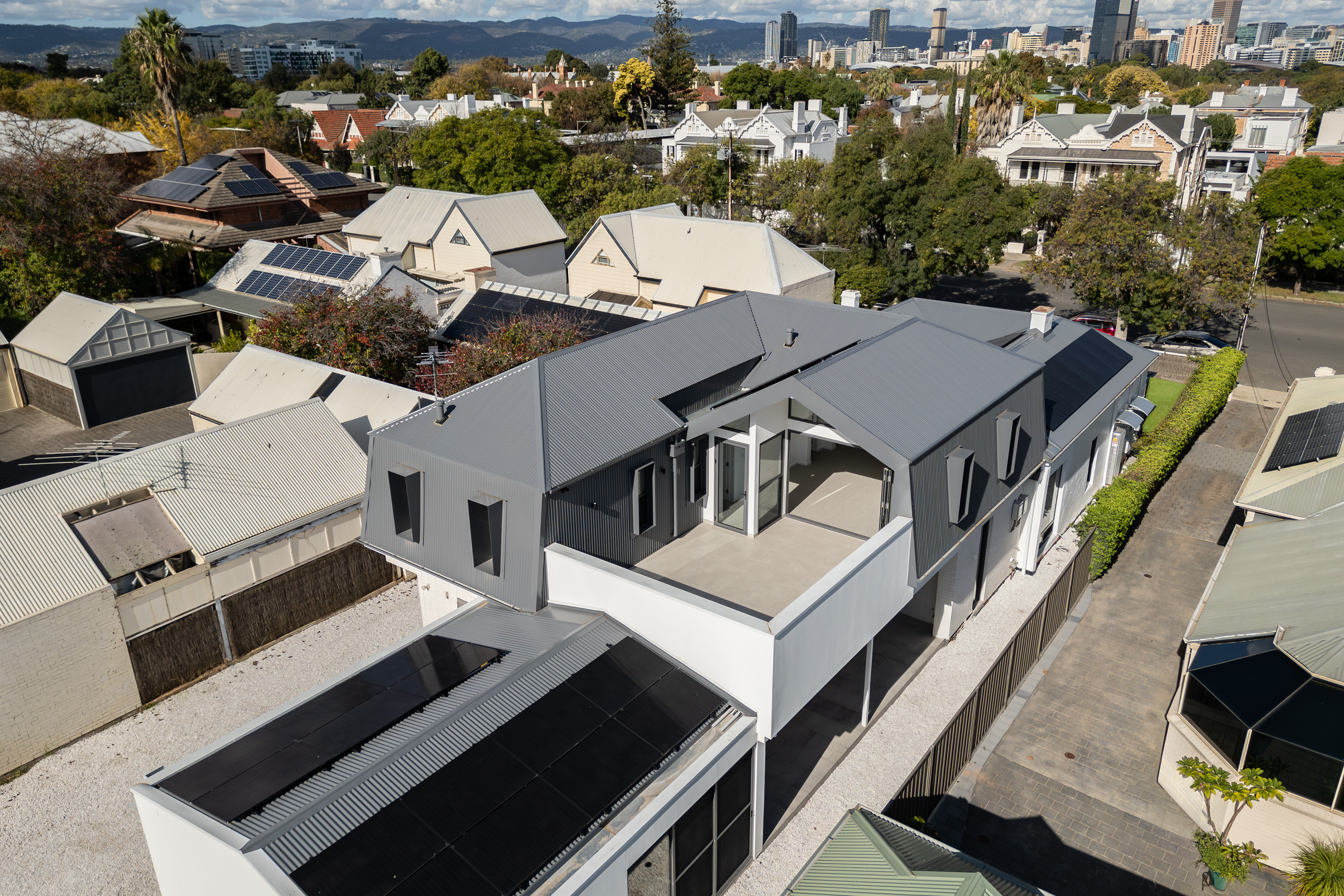 Aerial view of the restored villa and contemporary extension at 54 North Adelaide, with the city skyline beyond