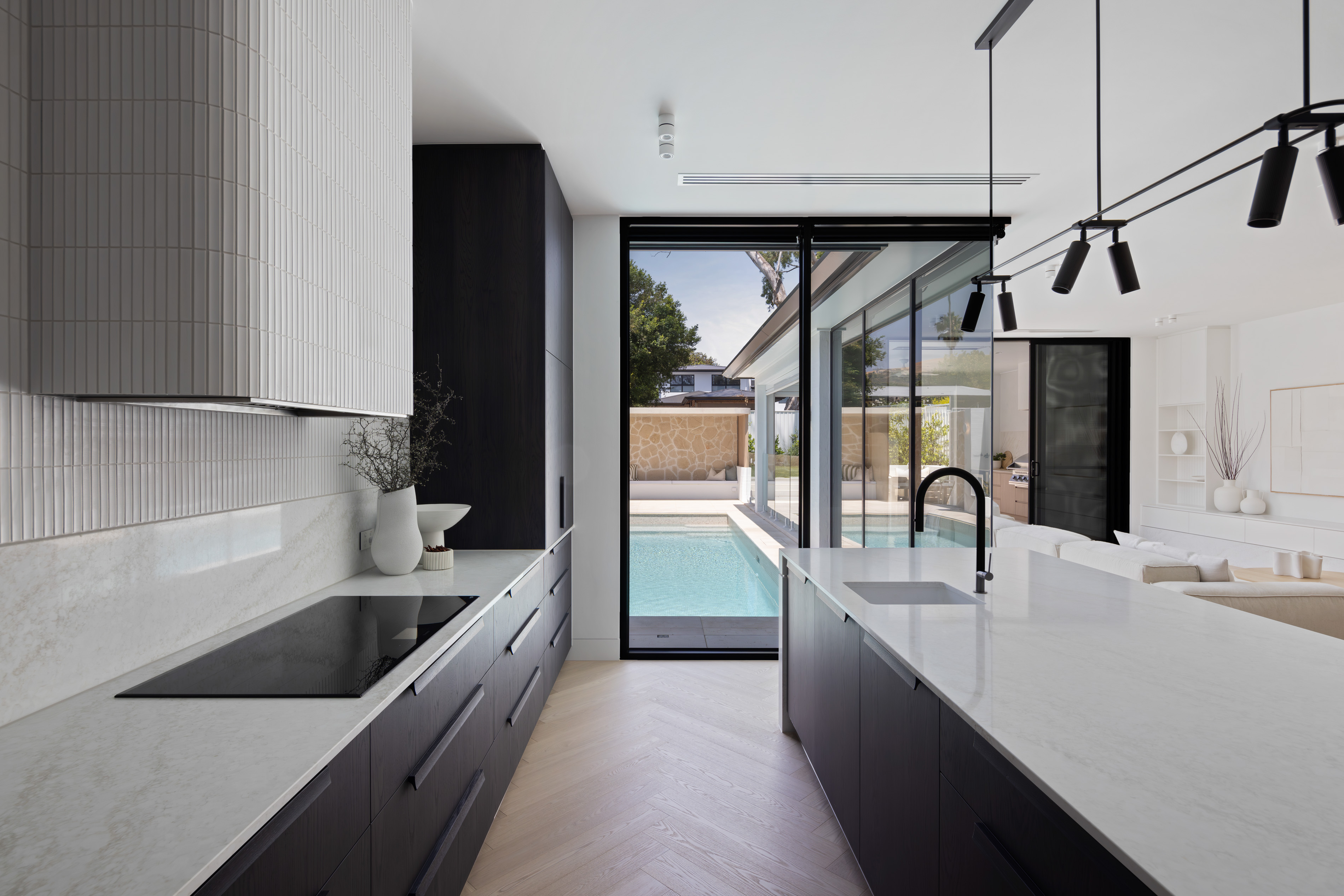 Contemporary kitchen with stone benchtops, dark cabinetry and a view through to the pool