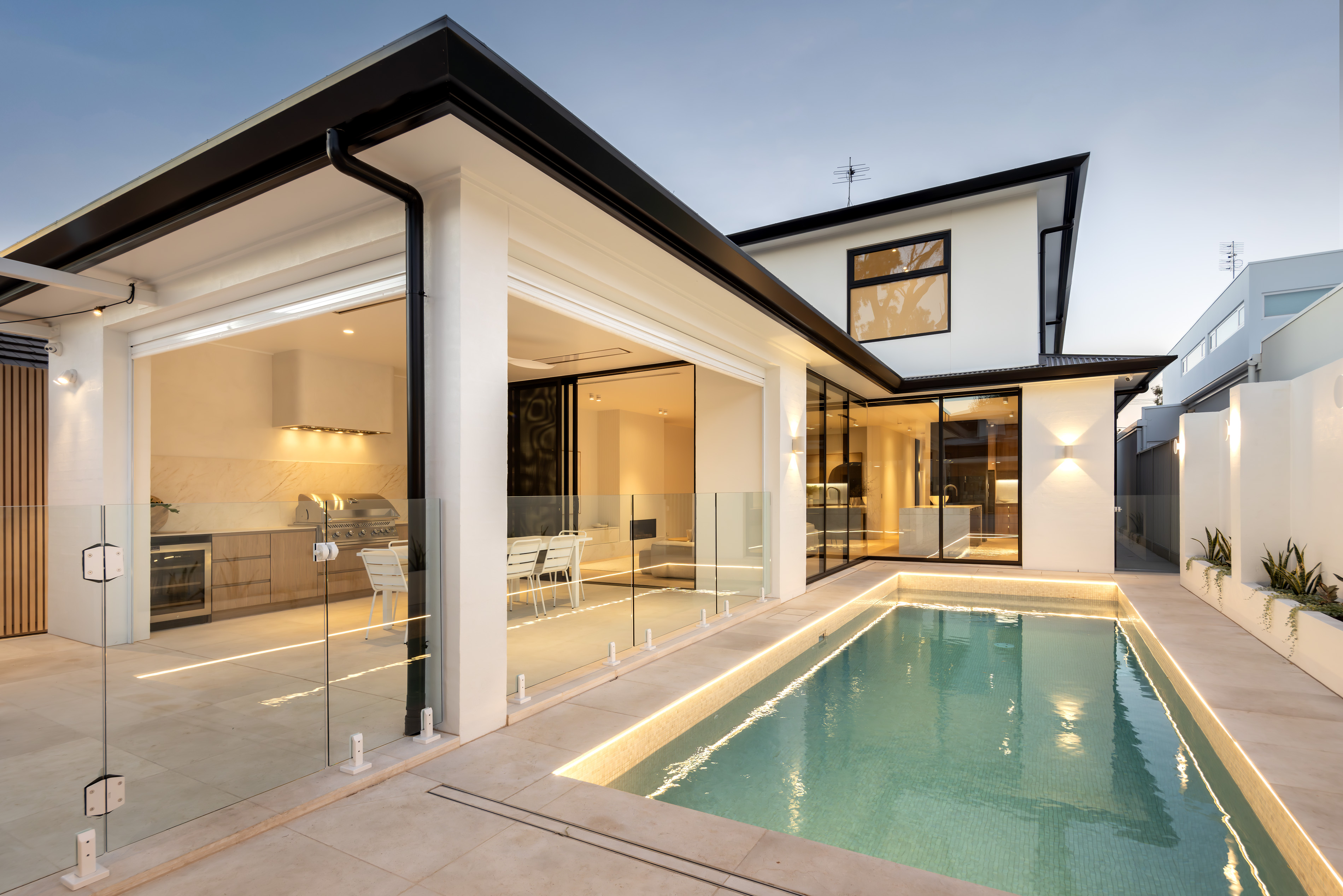 Covered alfresco and lit lap pool at dusk, with stacking glass doors opening the kitchen and living areas to the courtyard at 9 Netherby