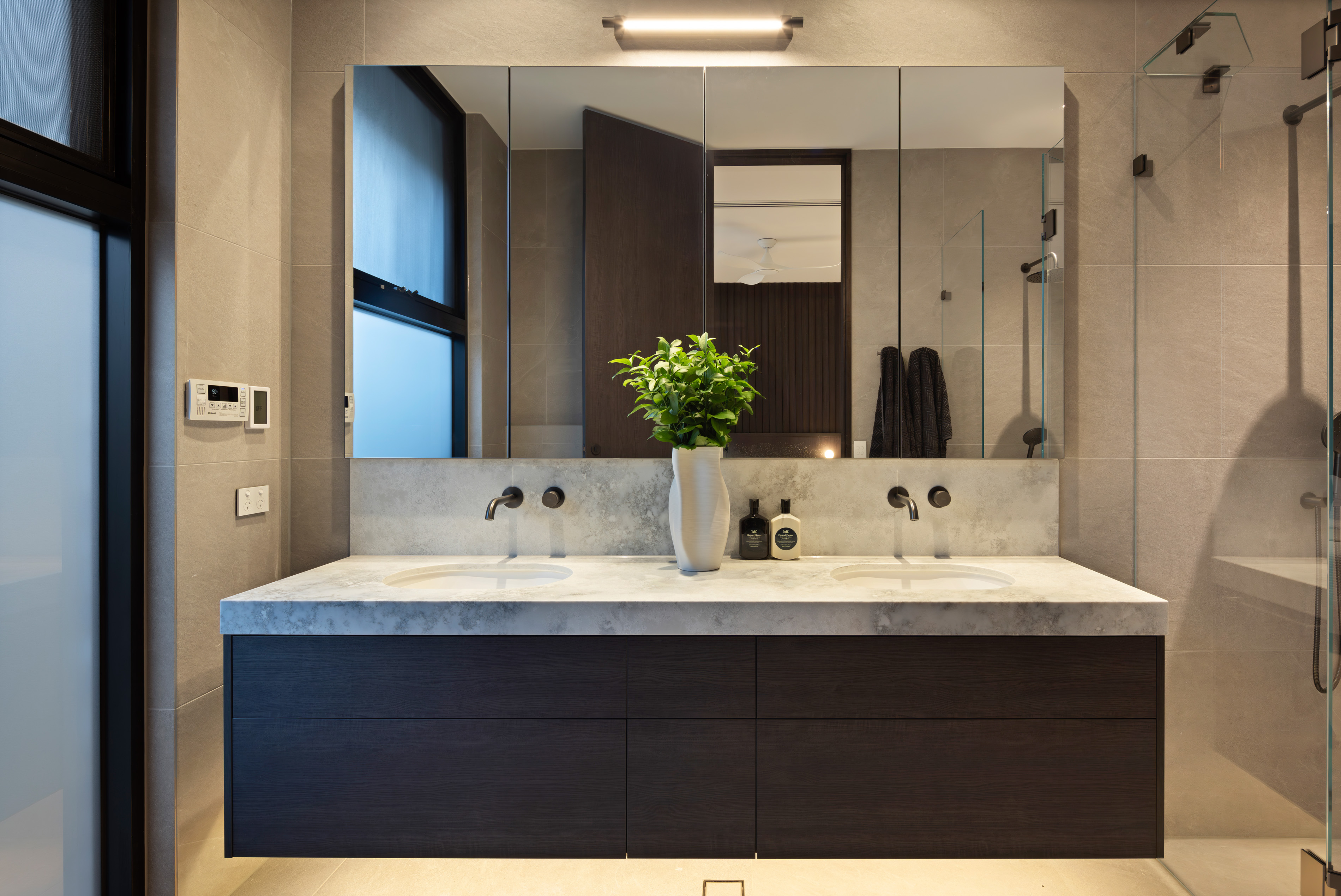 Bathroom with stone-topped double vanity, mirrored cabinetry and walk-in shower