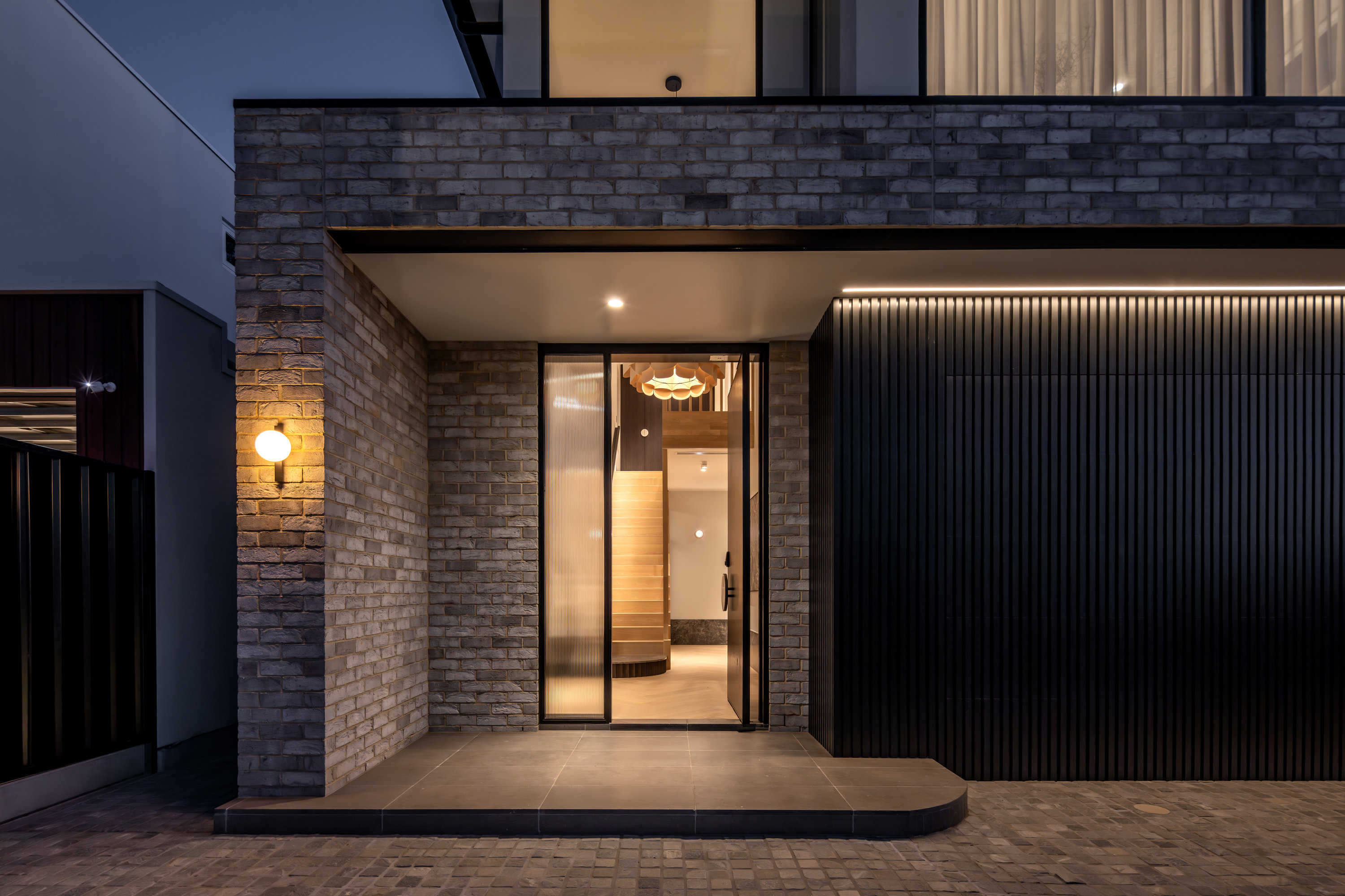 Entry portico lit at dusk with black battened garage door and paved driveway at 9 Netherby