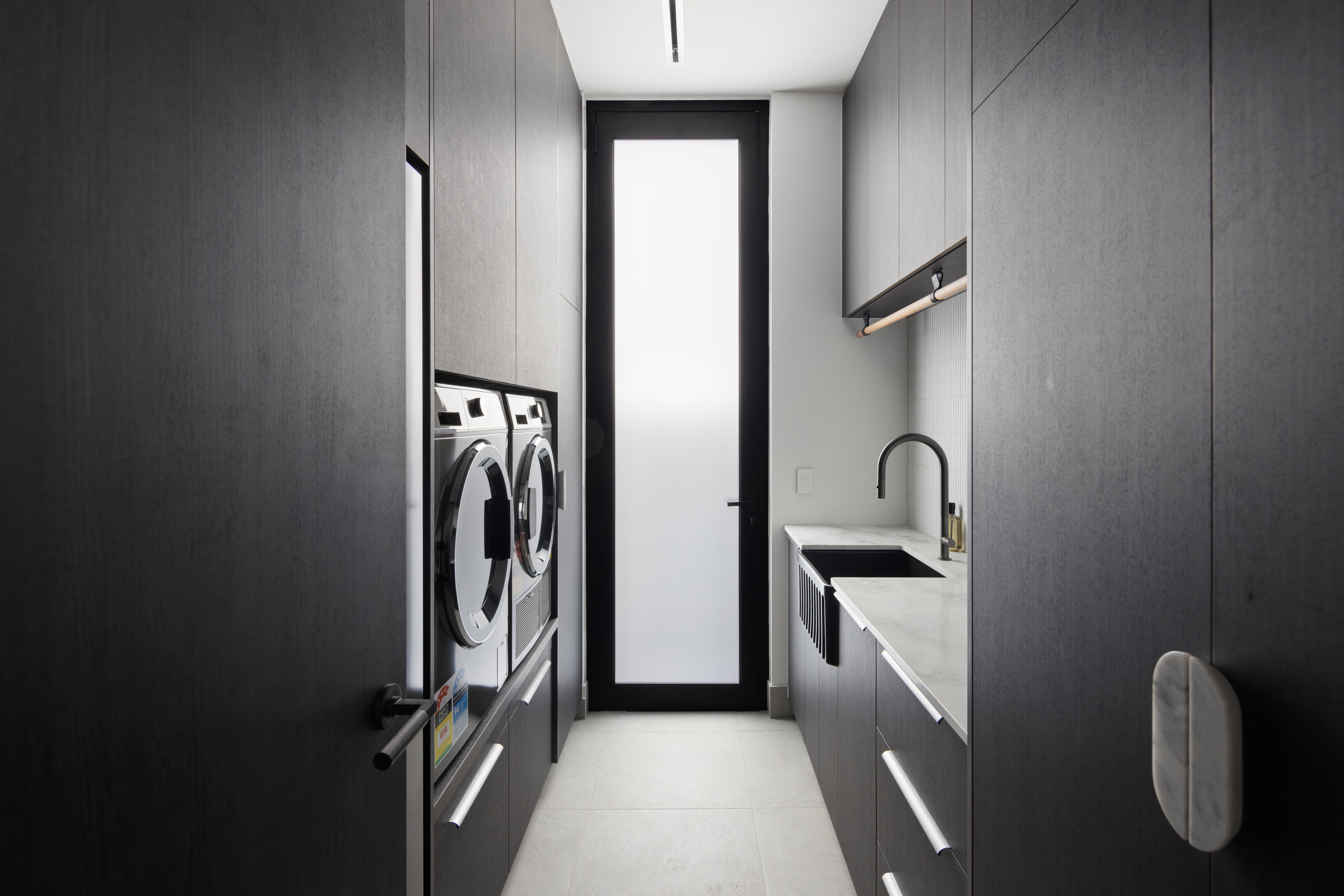 Laundry with dark timber joinery, stone benchtop and black tapware at 9 Netherby