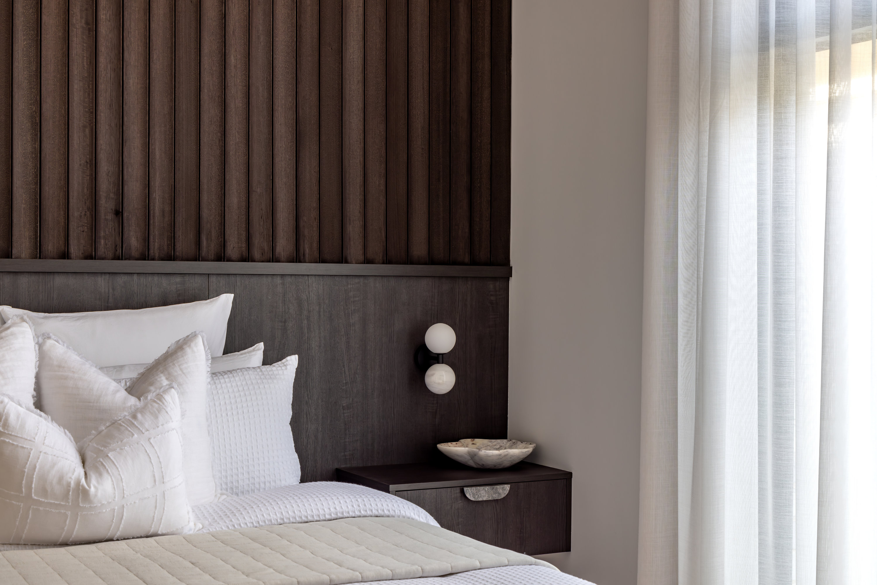 Main bedroom with a fluted dark timber bedhead wall and floating bedside shelf at 9 Netherby