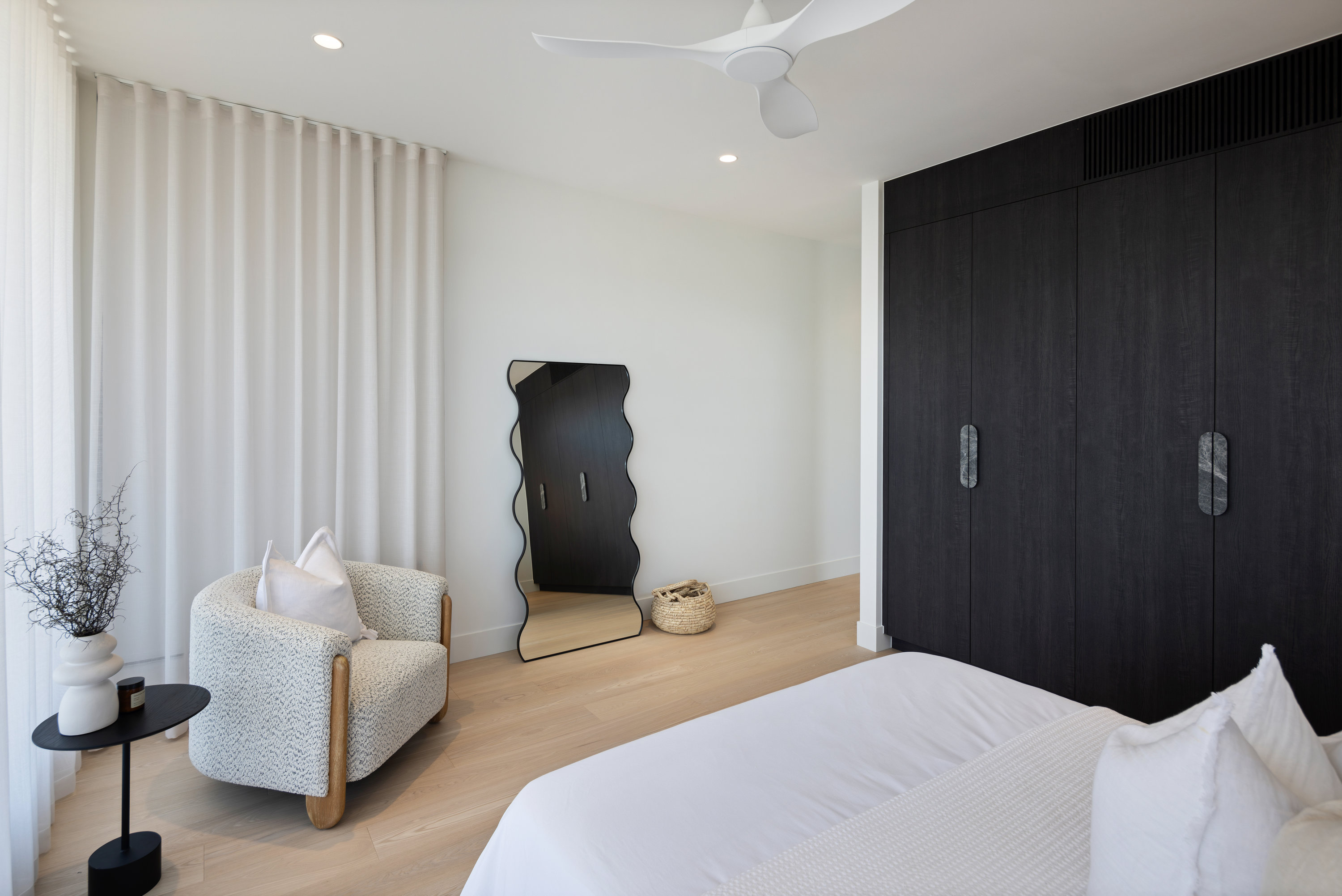 Bedroom with black timber wardrobe doors, boucle armchair and full-length mirror at 9 Netherby