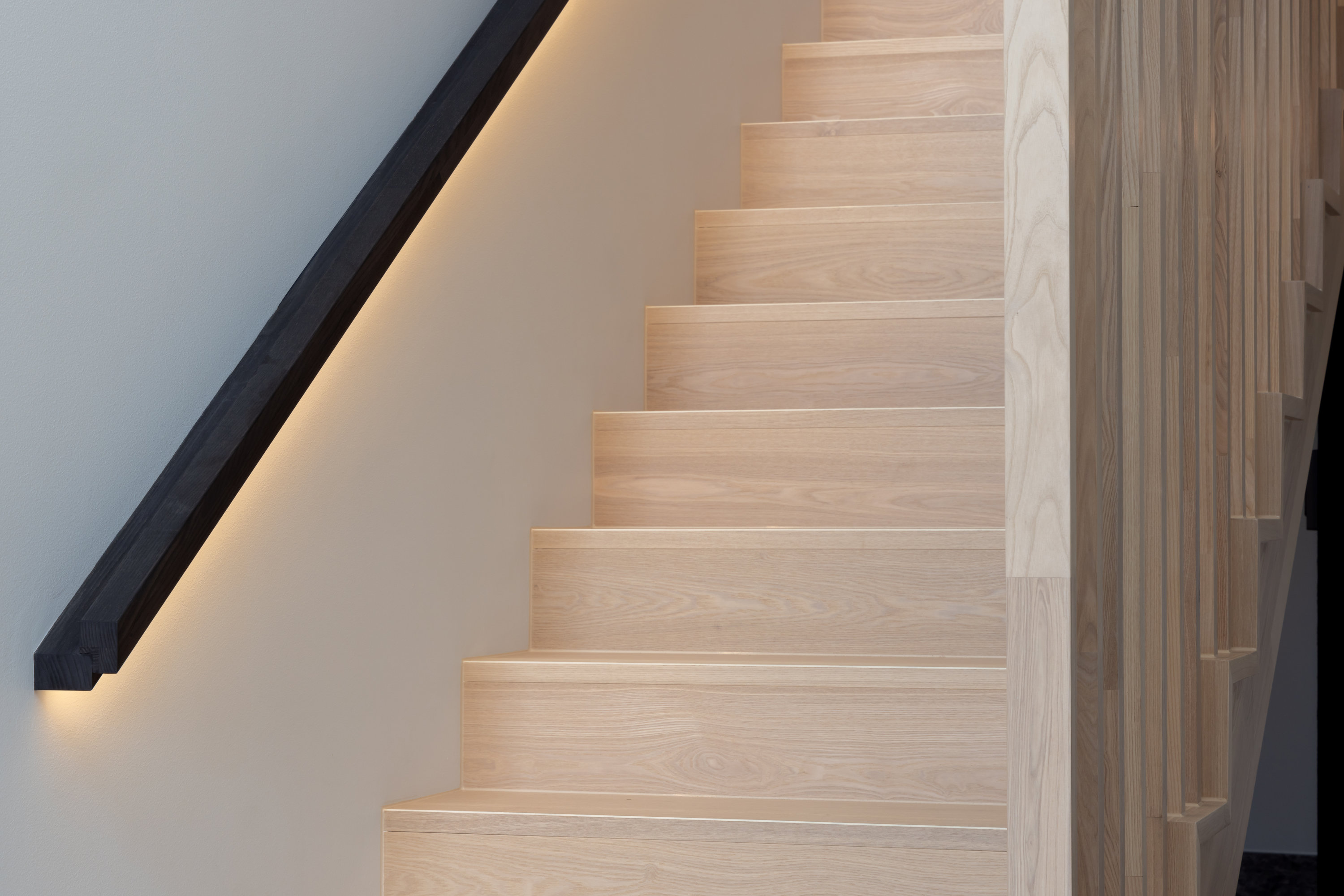 Oak stair treads with a black handrail and concealed strip lighting at 9 Netherby
