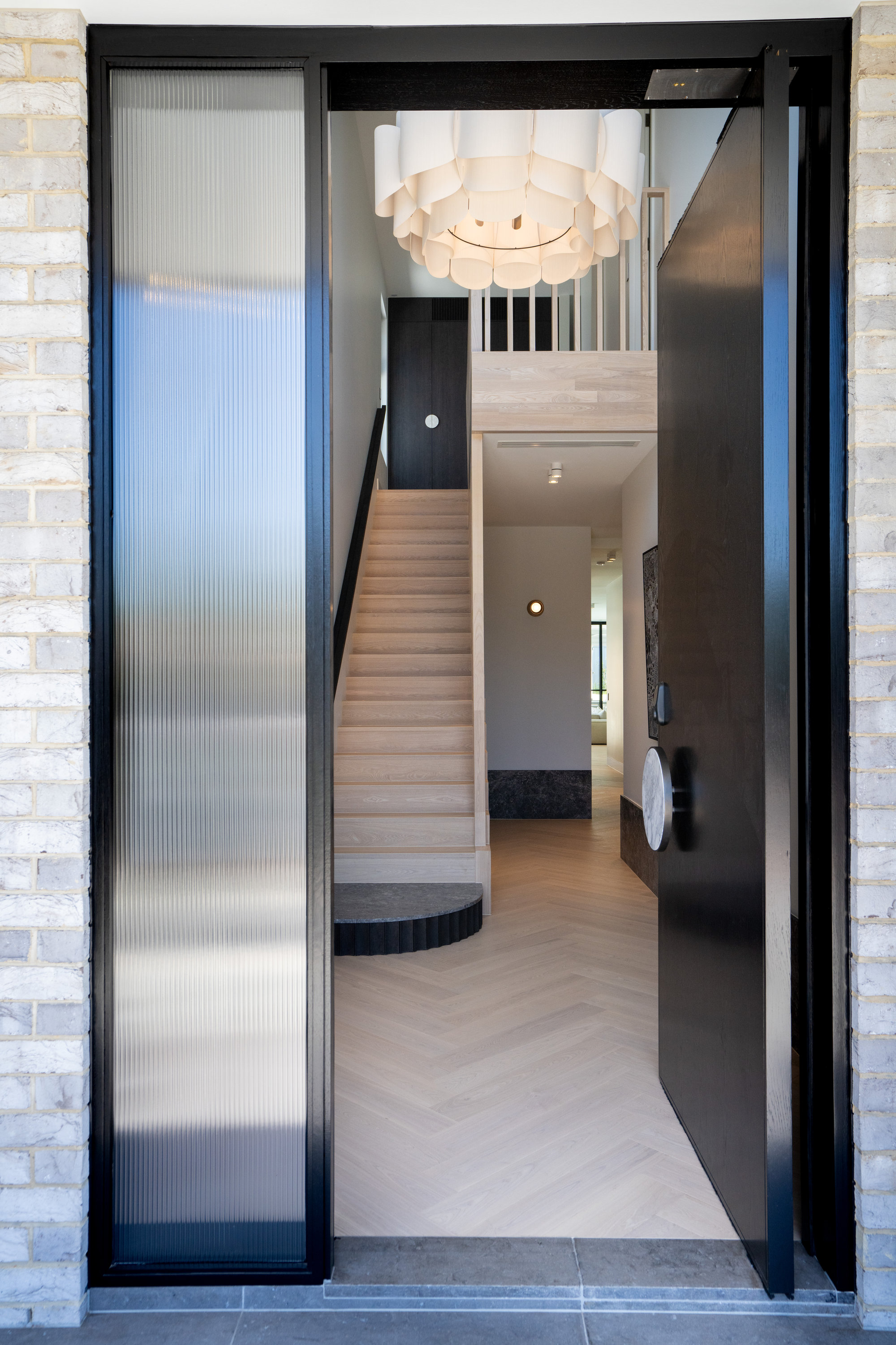 View through the open pivot door to the entry hall, sculptural pendant and oak stair at 9 Netherby