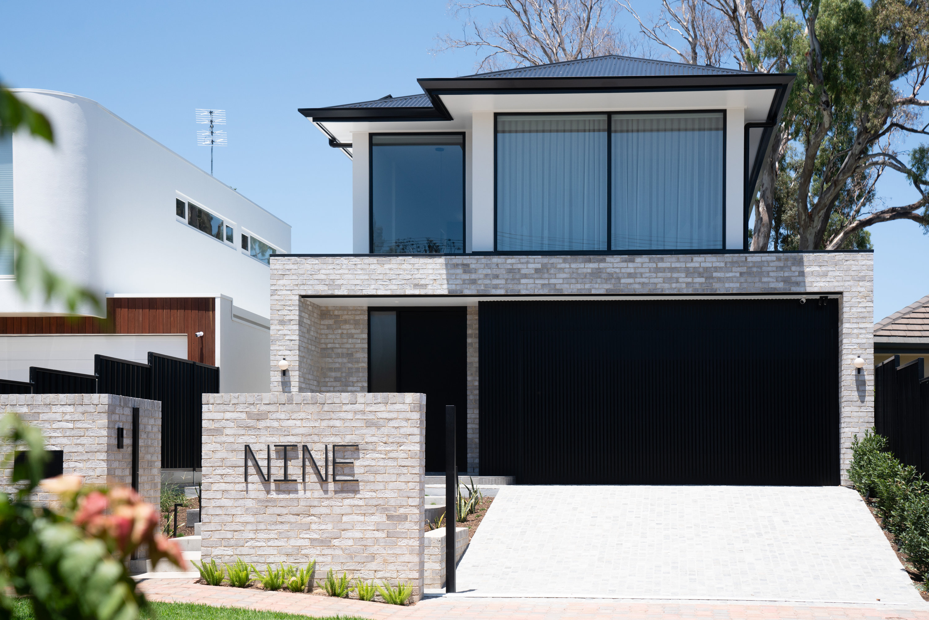 Brick and rendered street elevation with black garage door and landscaped entry at 9 Netherby