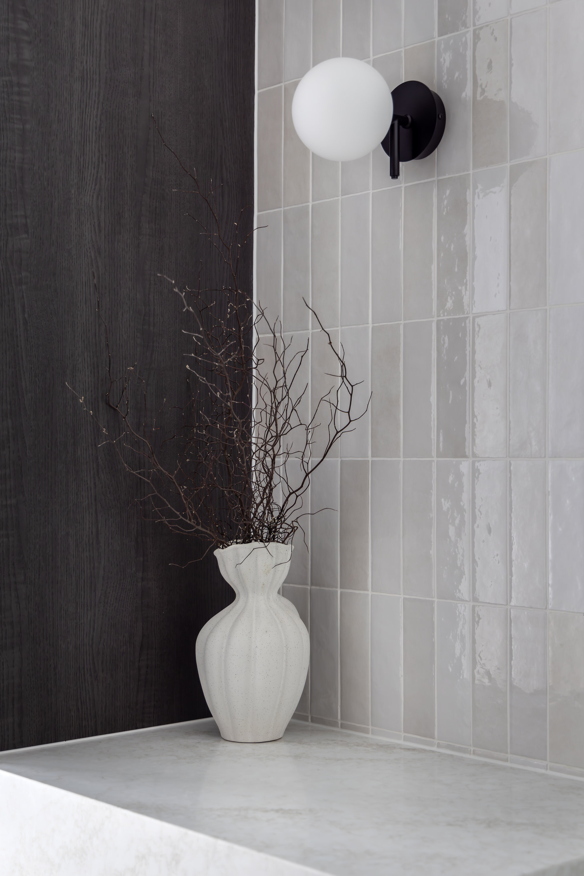 Black globe wall light and a dried arrangement against glazed tiling and dark timber cabinetry at 9 Netherby