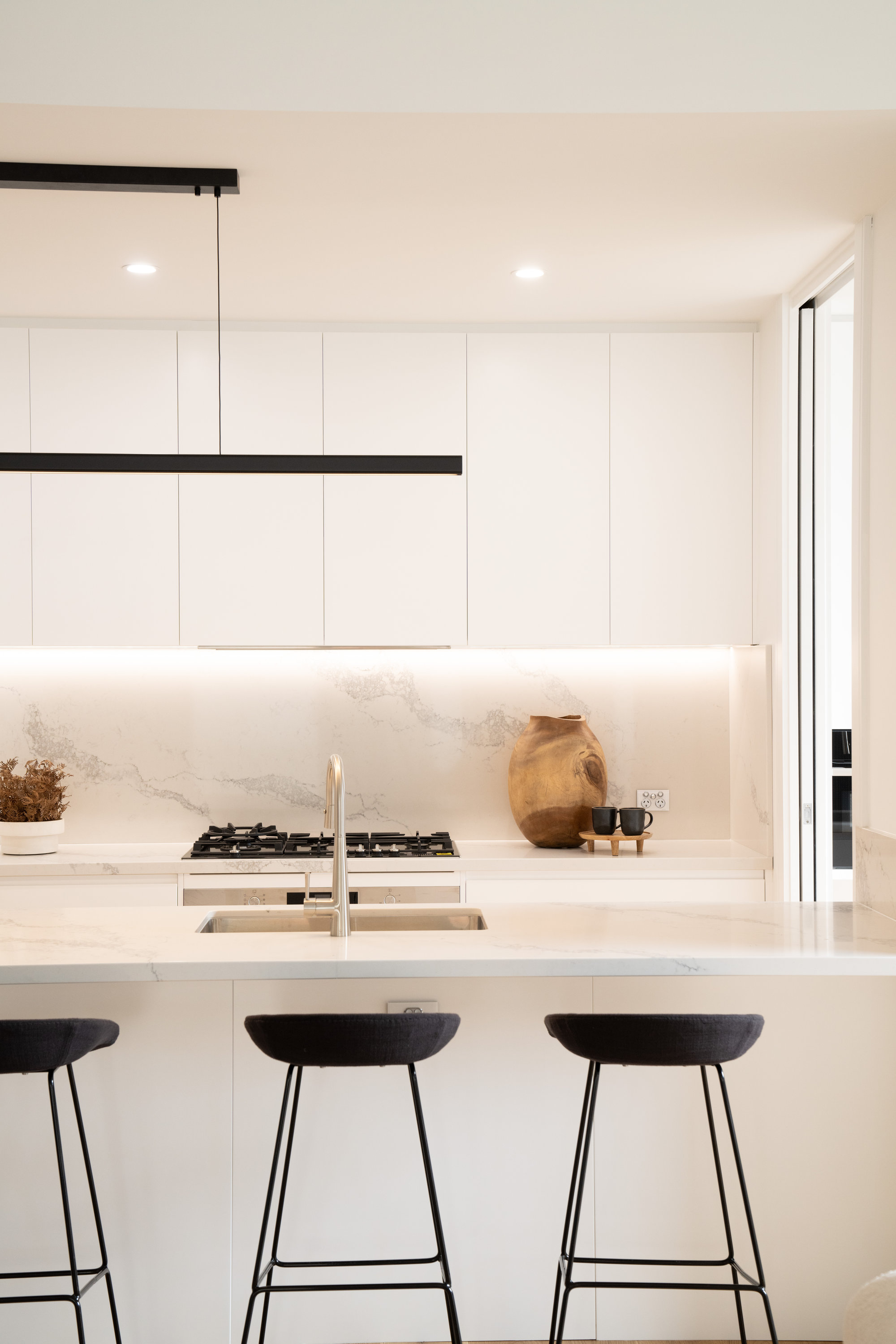 Kitchen with marble splashback, stone island bench and black linear pendant at 24 Wattle Park