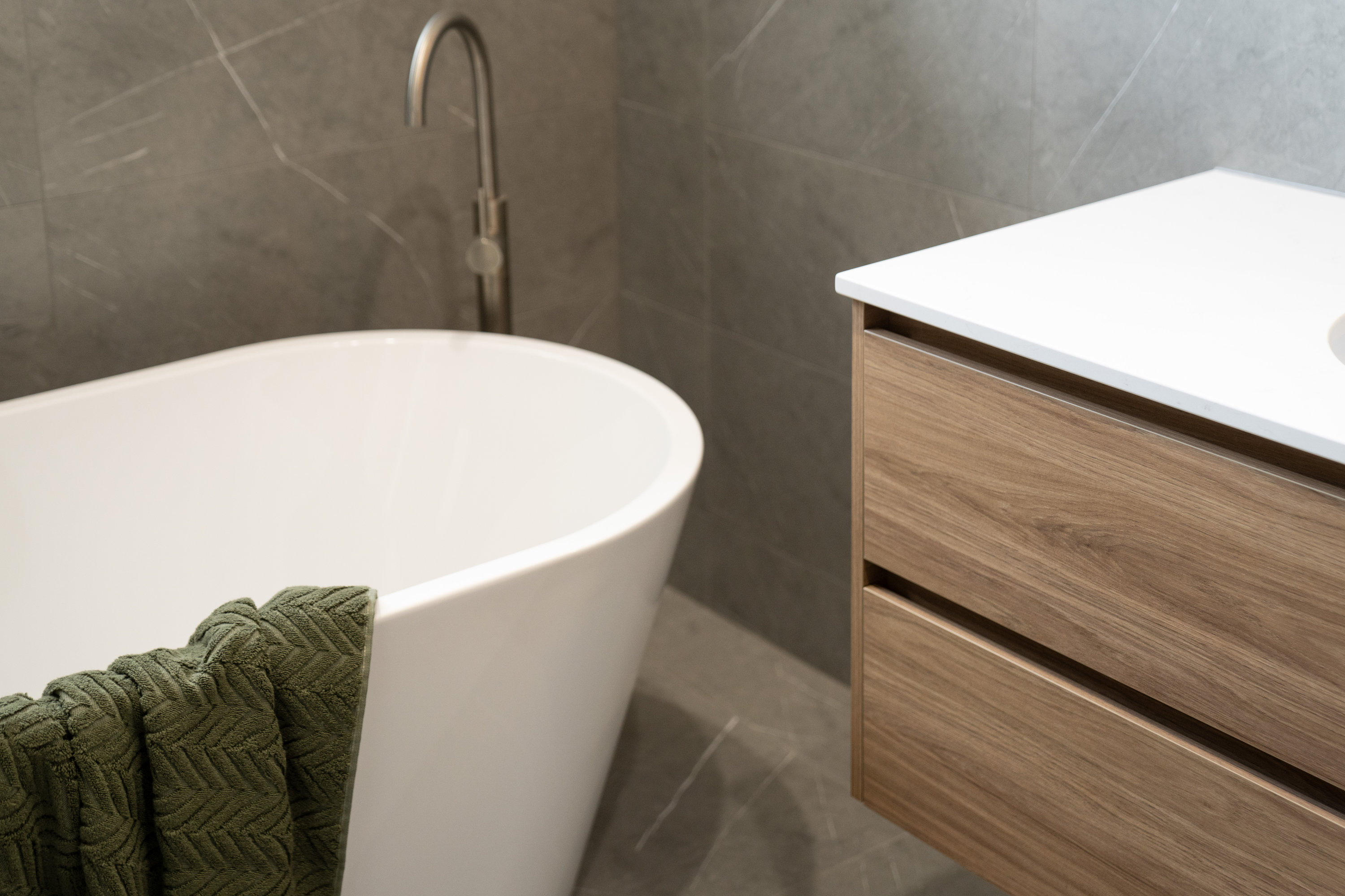 Freestanding bath beside a timber vanity with stone-look tiling at 24 Wattle Park