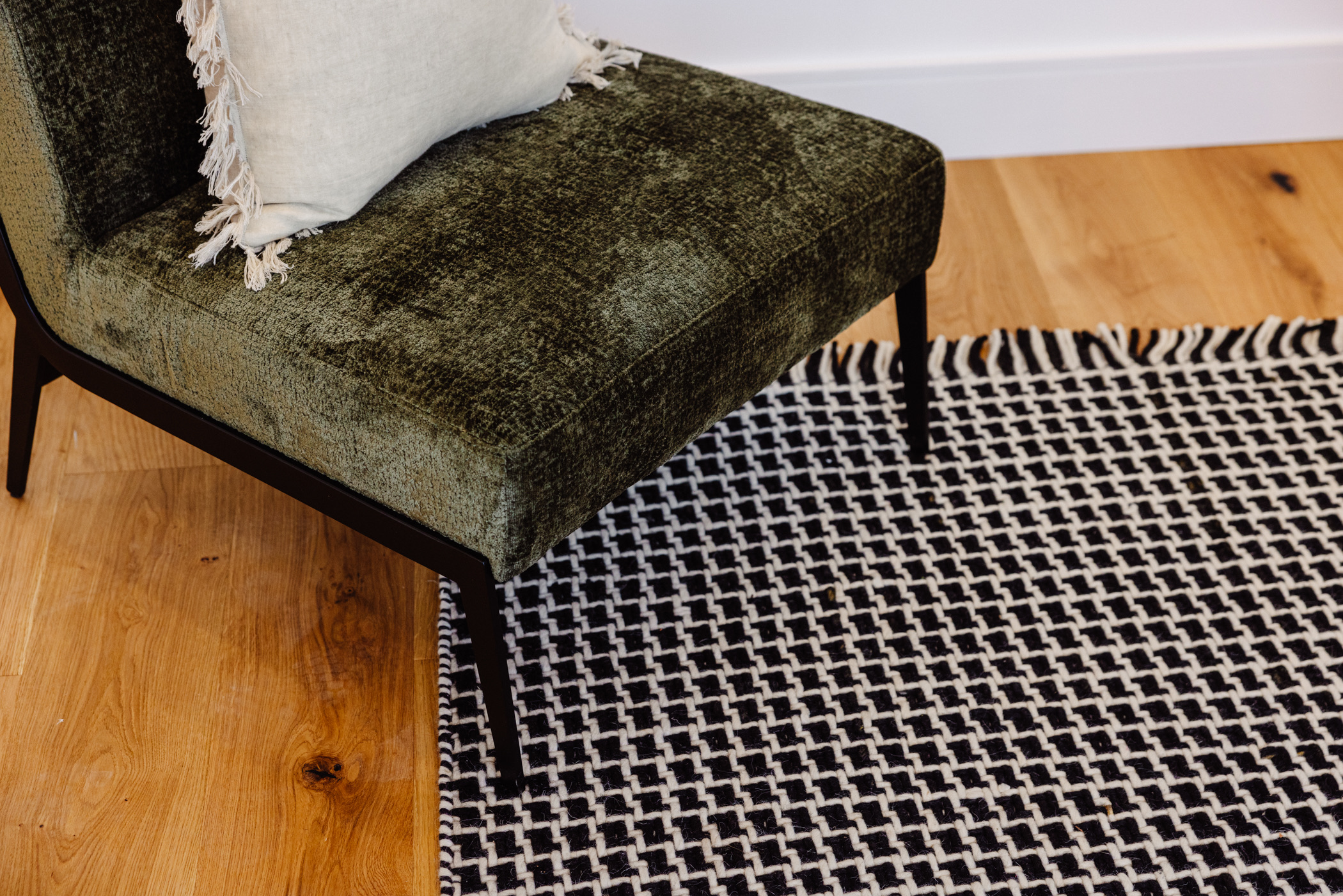 Olive velvet occasional chair with a linen cushion on a monochrome woven rug over oak flooring at 24 Wattle Park