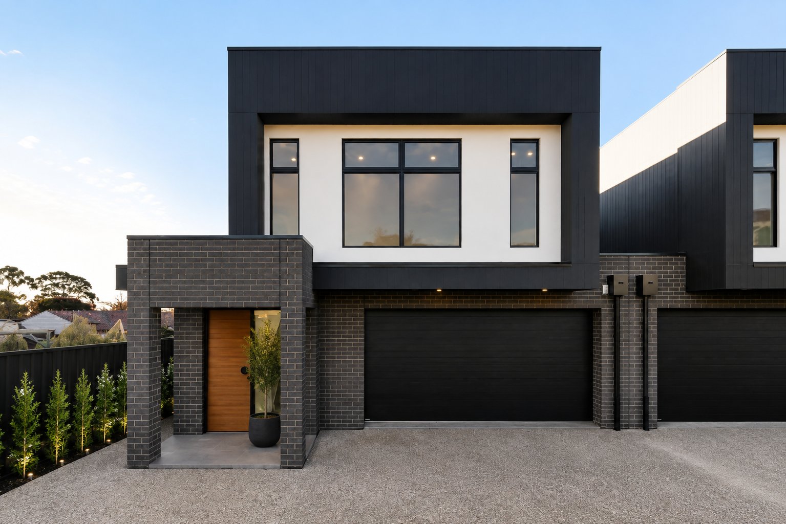 Street elevation of the completed dwellings with dark cladding, brick entry and black garage doors at 1 Magill