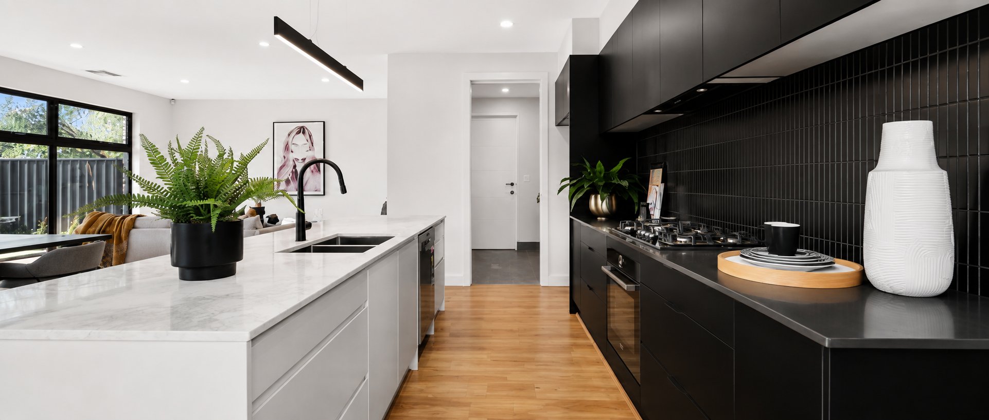 Kitchen with a stone island bench, black vertical tile splashback and oak flooring running through to the entry at 1 Magill