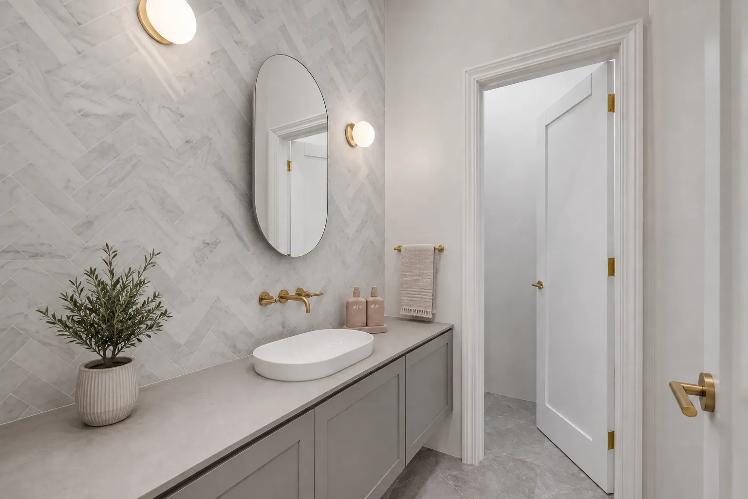 Powder room with herringbone marble wall, oval mirror and brass wall-mounted tapware at 84 Toorak Gardens