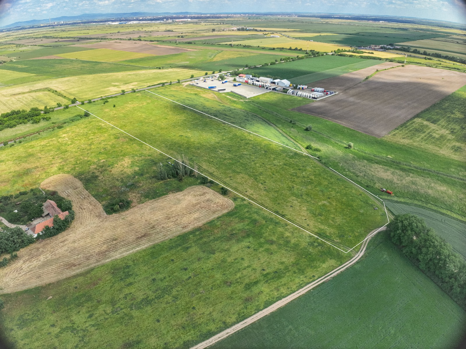 Aerial view of farmland with a river, green fields, road, storage area, and rural houses.