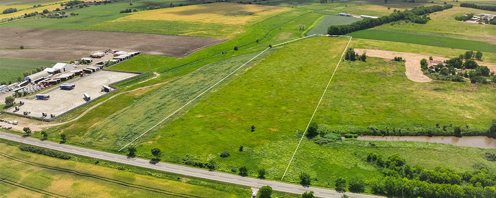 Aerial view of green farmland bordered by a road and storage area with trucks and equipment.