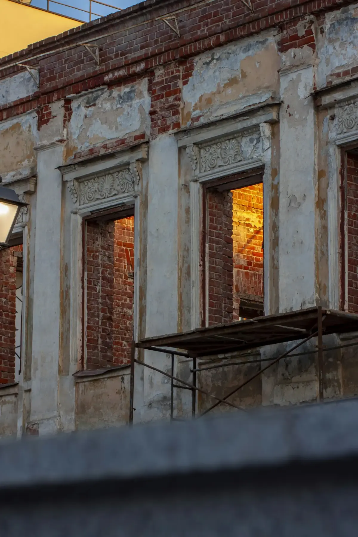 Historic brick facade under restoration with scaffolding and amber light in the windows